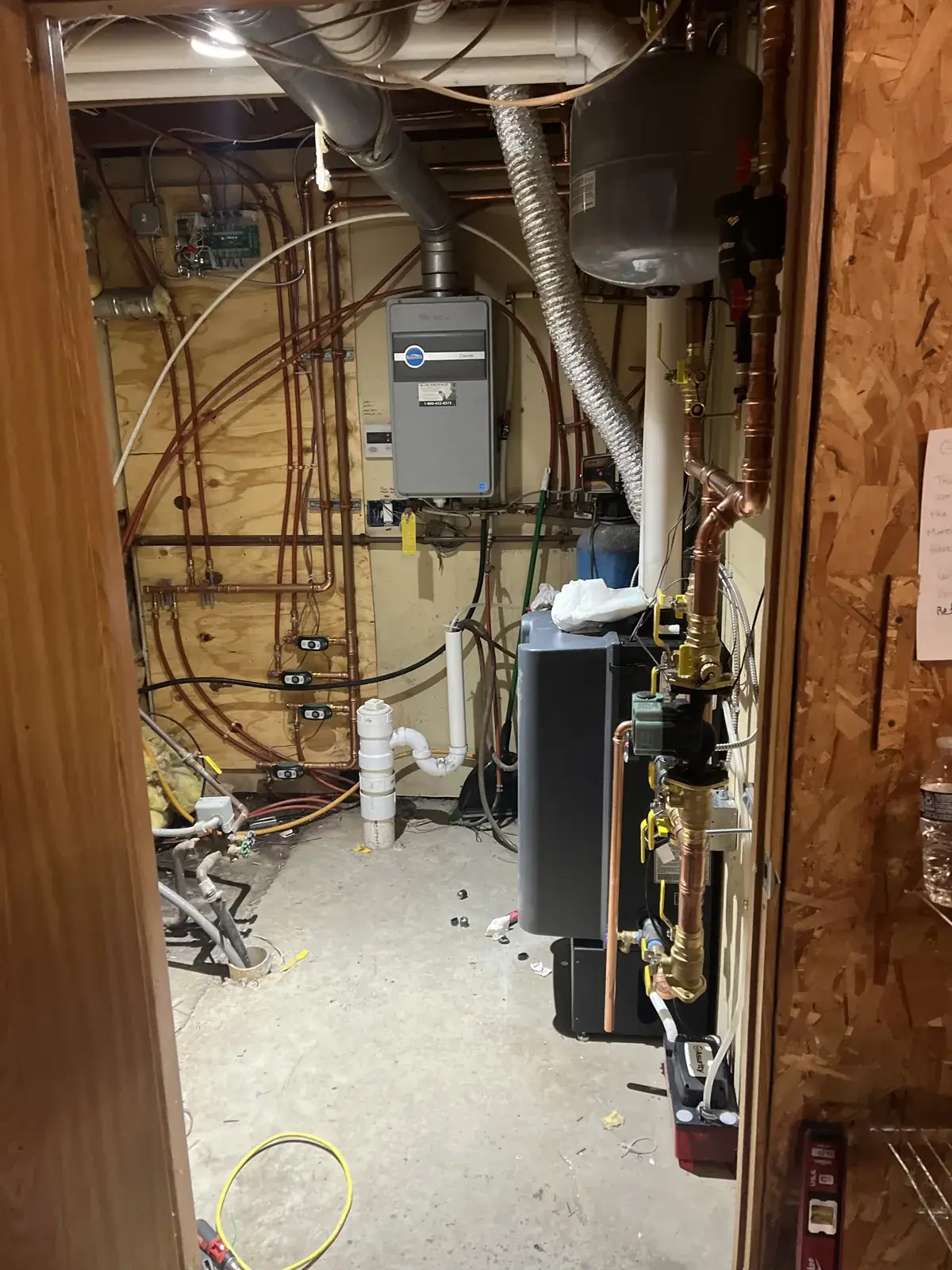 Wall-hung condensing boiler and in-floor heat loops piped in a utility room, with the expansion tank and manifold set