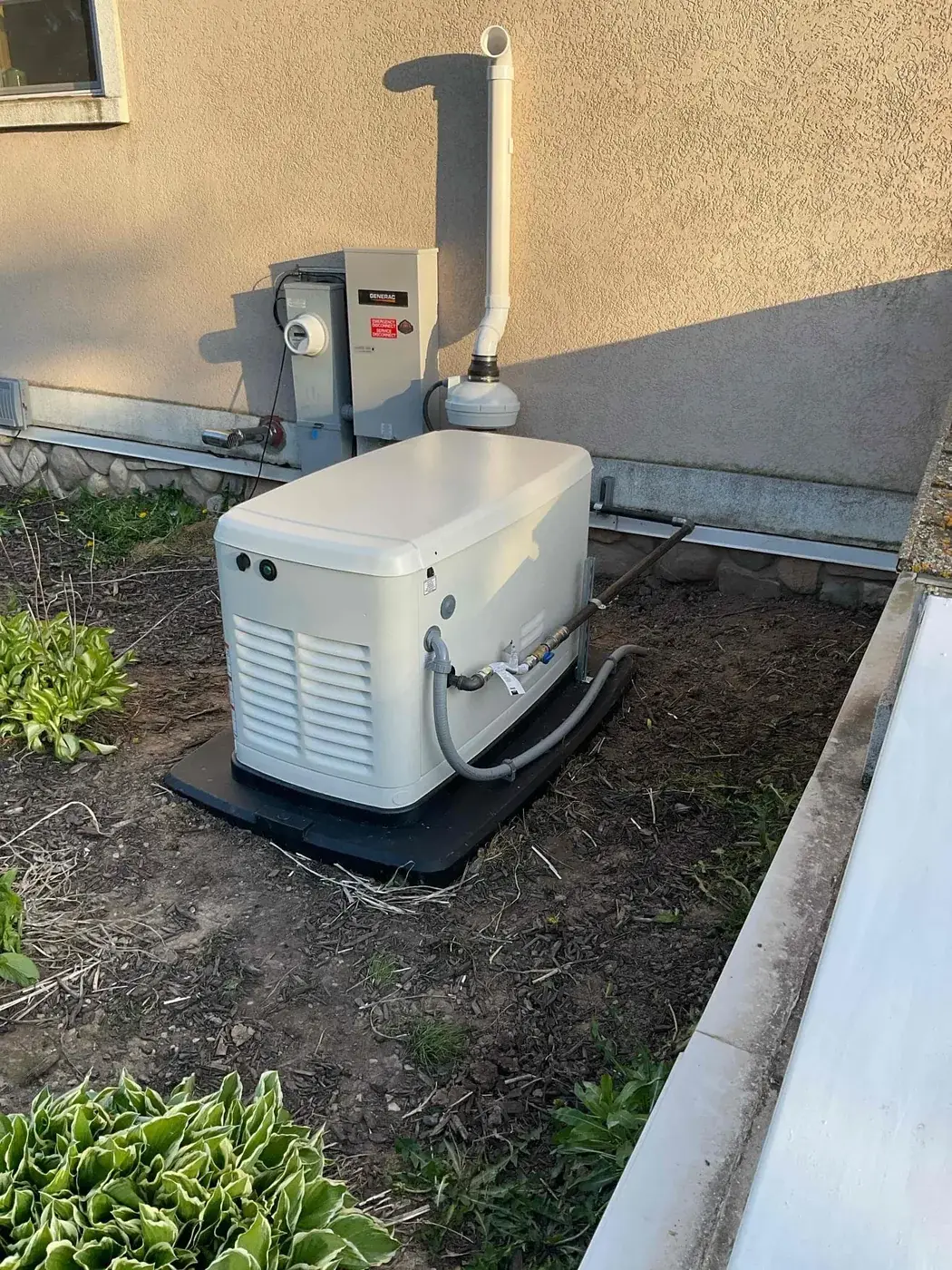 Standby generator installed tight to the house with its transfer switch alongside