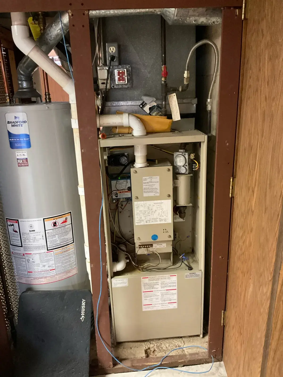 Before — an aging closet furnace with its data plate and old venting